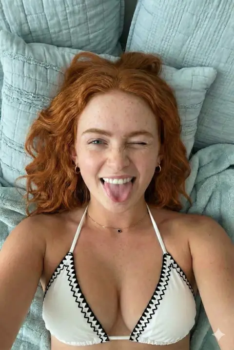 A blond bikini girl playfully sticking out her tongue from an overhead shot