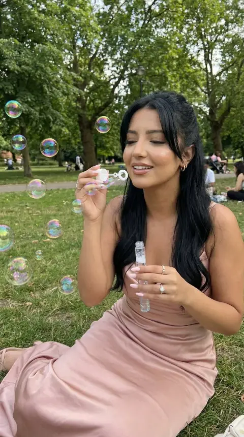A girl in a pink skirt in the green field blows dreamy colorful bubbles
