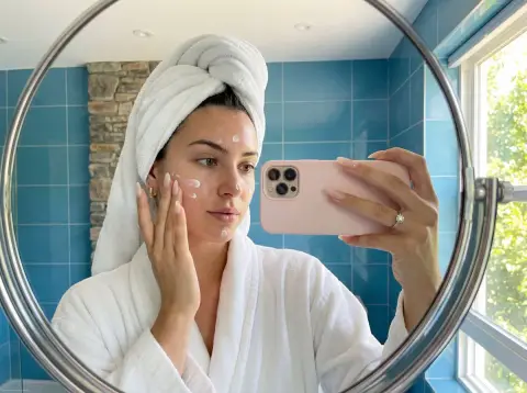 A girl taking a selfie in the mirror with skin care in the bathroom after bathing in the fresh morning light