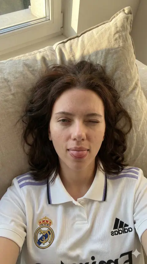 A girl taking a playful selfie in a Real Madrid jersey under the morning light