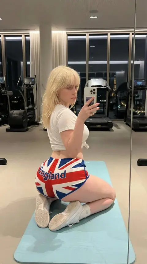A girl with an extreme waist-to-hip ratio takes a selfie in the mirror in the Paris night view gym