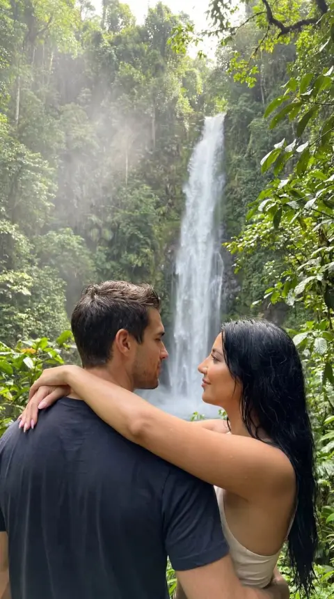 A hyper-realistic tropical rainforest couple embracing each other in the mist of a waterfall