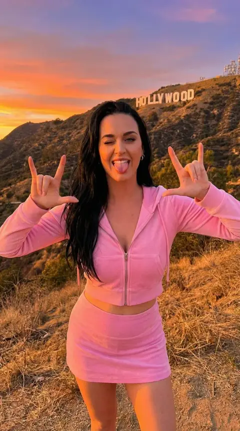 A playful girl in red making the LA sign at the foot of the Hollywood Hills
