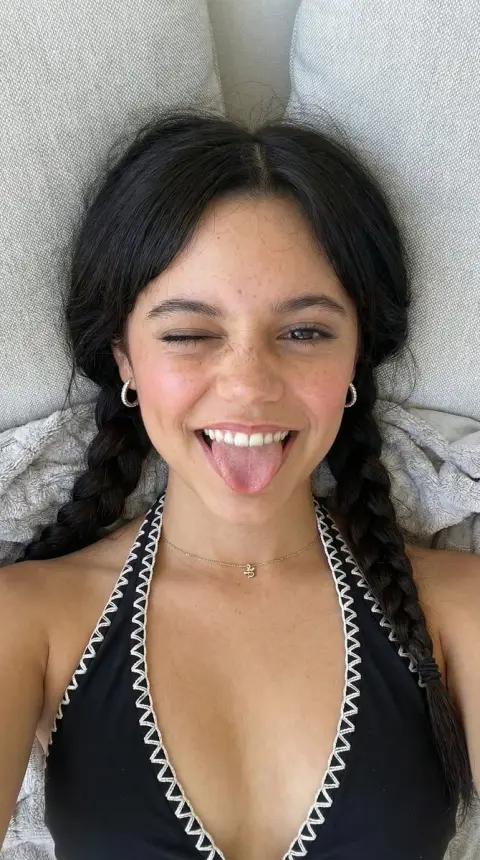 A top shot of a girl in an orange swimsuit playfully winking and sticking out her tongue