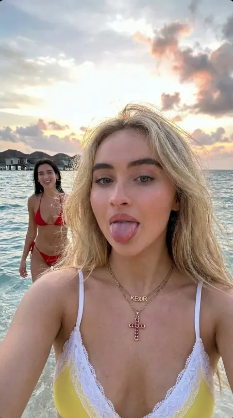 Blonde girl takes a playful selfie with Dua Lipa on the beach in the Maldives