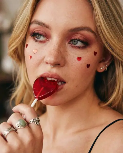 Blushing girl biting a heart-shaped lollipop