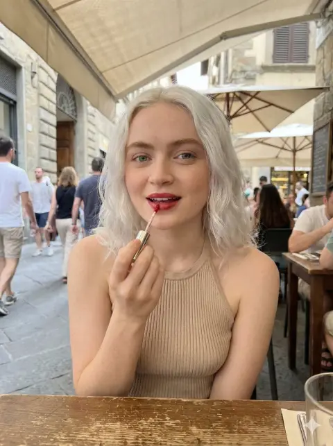 Elegant girl applying red lips in a street corner cafe in the afternoon