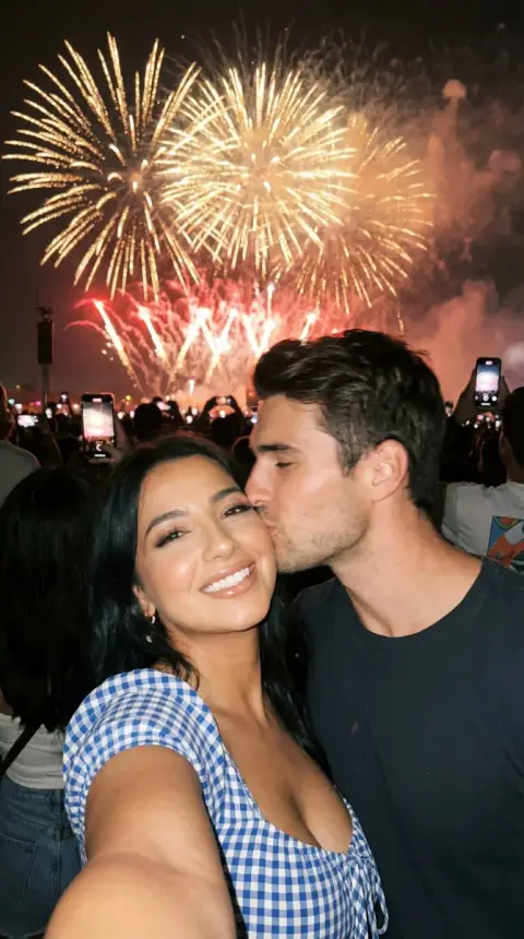 Night selfie of couple kissing intimately under bright fireworks