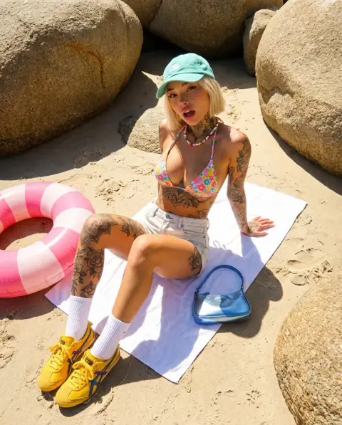 Stylish tattooed girl wearing sneakers among rocks in sunshine