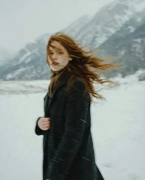 The poetic moment of a lonely figure in the snow with long auburn hair blowing in the wind