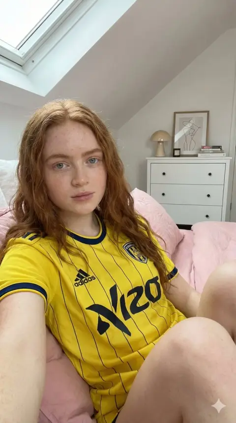 The red-haired girl wearing a yellow and blue jersey in the sunshine loft
